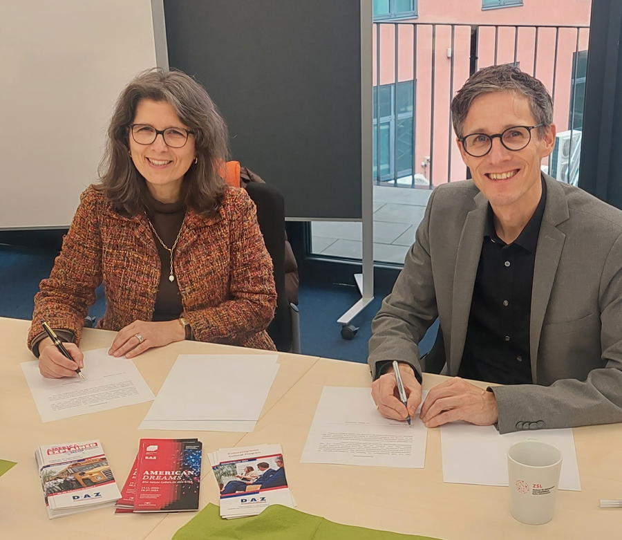 Frau Pyka und Herr Dr. Bläsi sitzen gemeinsam unterschreibend an einem Tisch in der ZSL-Regionalstelle Stuttgart. 
