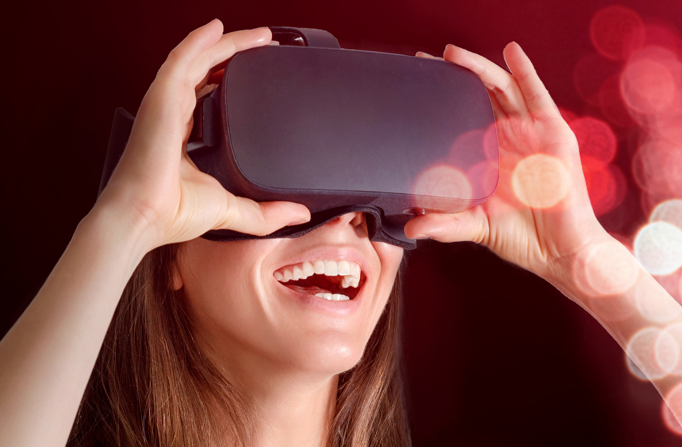 Lachende junge Frau mit VR-Brille vor rotem Hintergrund