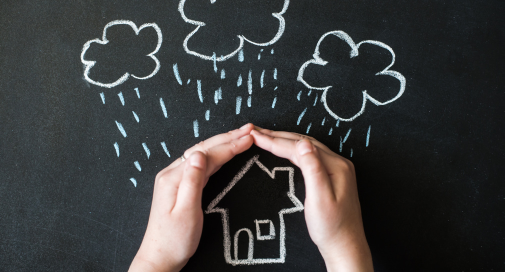 Link zur Seite Katastrophenschutz an Schulen (Symbolfoto: Hände schützen mit Kreide gezeichnetes Haus vor gezeichnetem Regen)