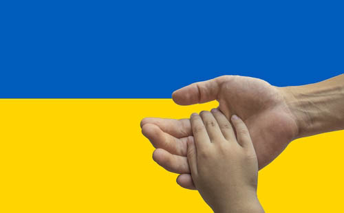 Foto: Kinderhand ruht in Erwachsenenhand, Hintergrund: ukrainische Flagge