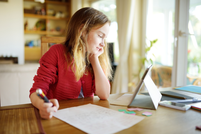 Schülerin vor Laptop und Arbeitsblatt am Esszimmertisch