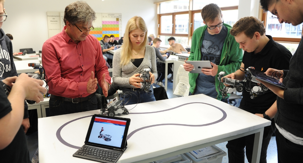 Foto: Berufsschullehrer und Schülerinnen und Schüler erproben einen Roboter