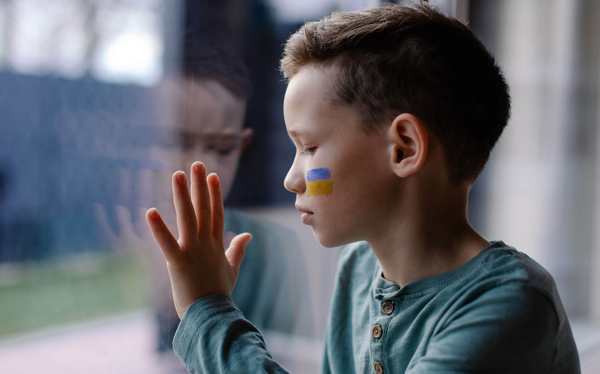 Foto: Junge am Fenster mit Ukraine-Flagge auf der Wange