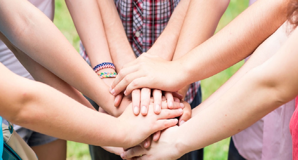 Foto: Jugendliche legen in der Mitte ihre Hände übereinander, um Gemeinschaft auszudrücken
