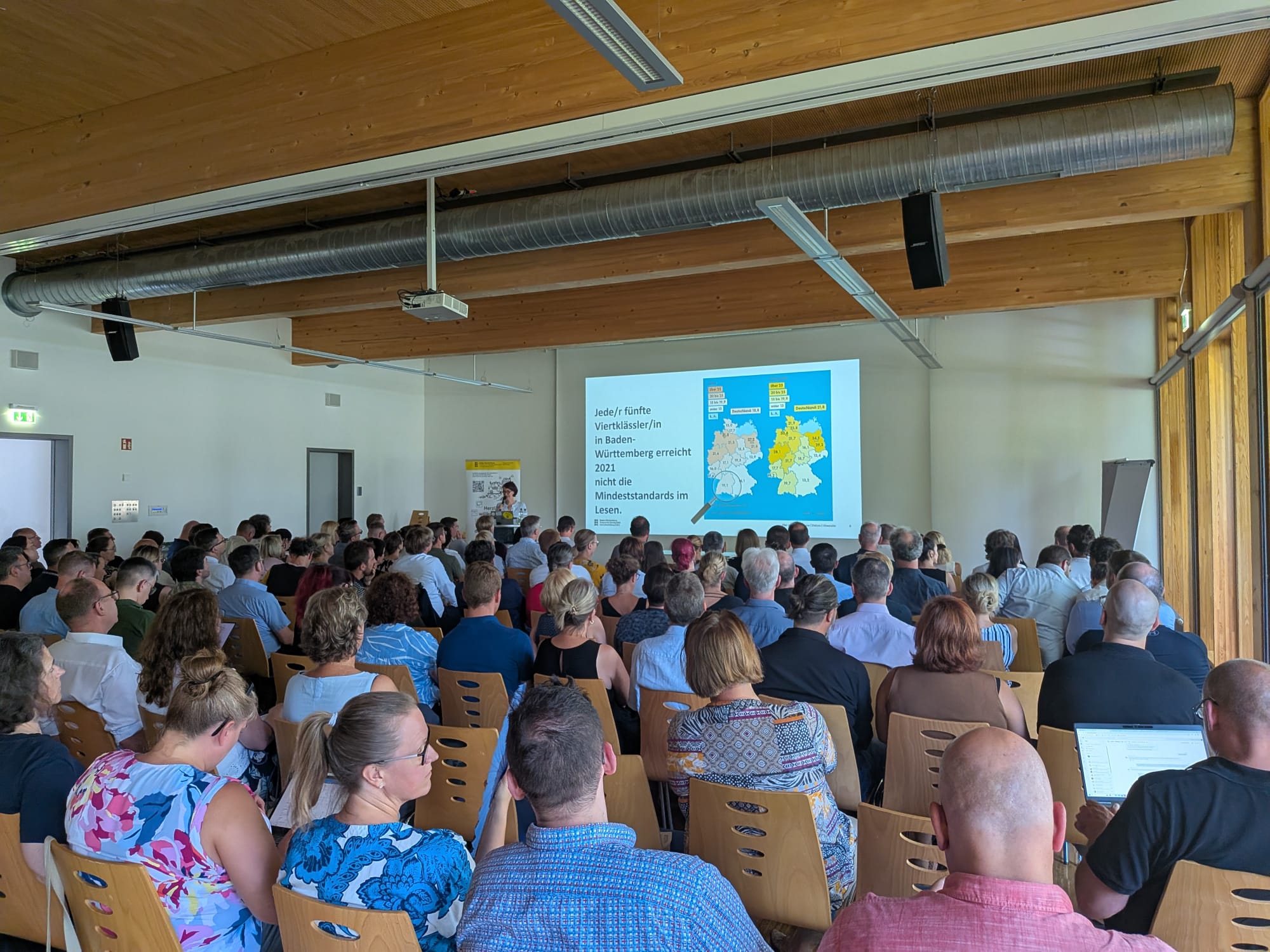 Teilnehmende einer Fachveranstaltung verfolgen einen Vortrag mit Präsentation in einem modernen Konferenzraum.