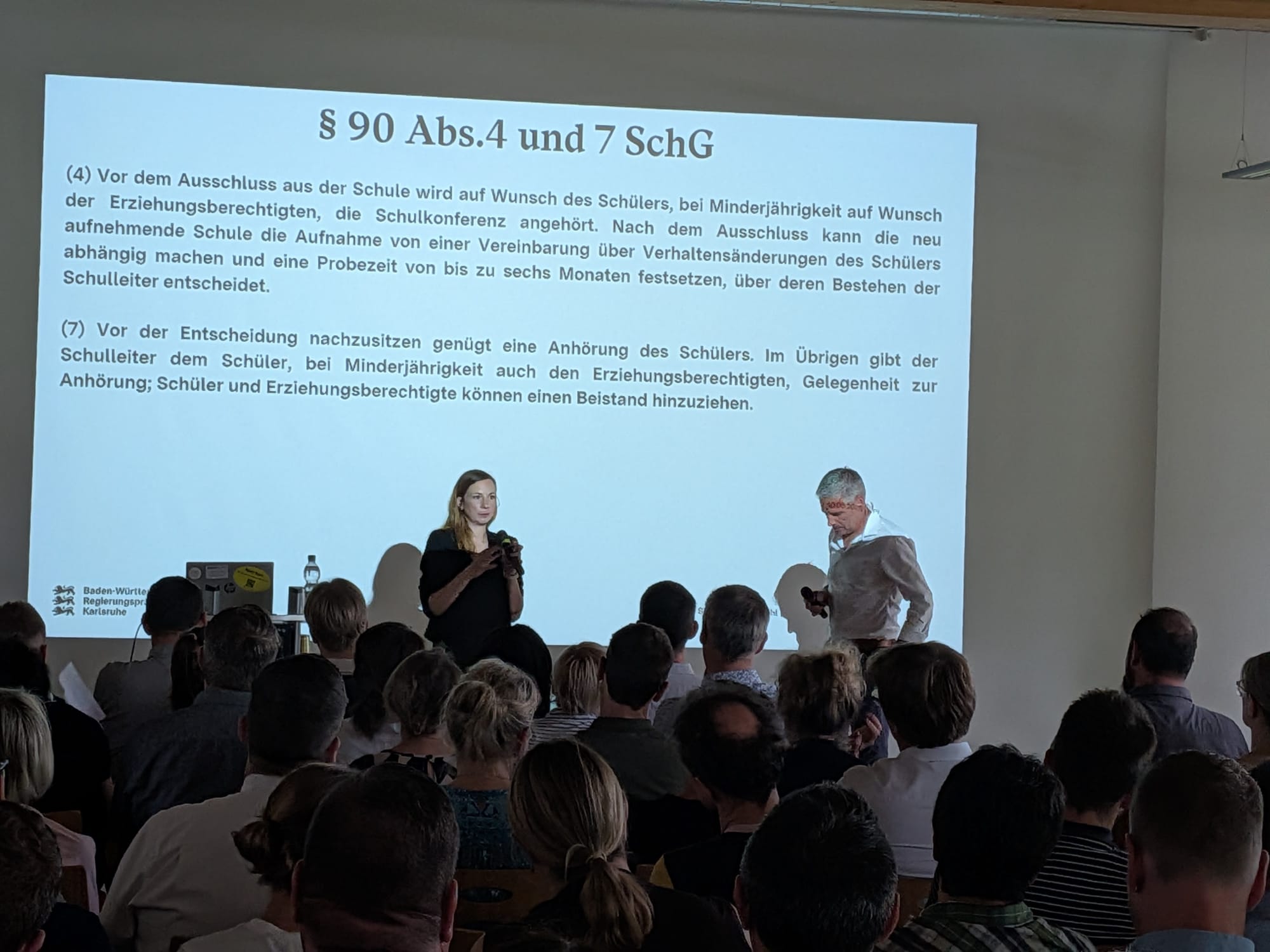 Teilnehmende einer Fachveranstaltung verfolgen einen Vortrag mit Präsentation in einem modernen Konferenzraum.