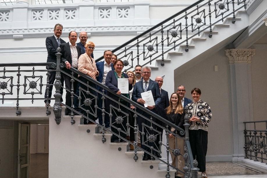Gruppenfoto: auf einer Treppe stehen dem Betrachter zugewandt vierzehn Personen, die lächeln. Unter anderem sind es folgende Personen: Links oben auf dem Treppenabsatz steht ZSL-Präsident Professor Dr. Thomas Riecke-Baulecke. Weiter unten auf der Treppe stehen Theresa Schopper, baden-württembergische Kultusministerin, und Uwe Bleich, Vorstand der Hector Stiftungen. Beide halten jeweils ein Exemplar Vereinbarung zur Verlängerung ihrer Zusammenarbeit mit den Hector Kinderakademien in Händen.