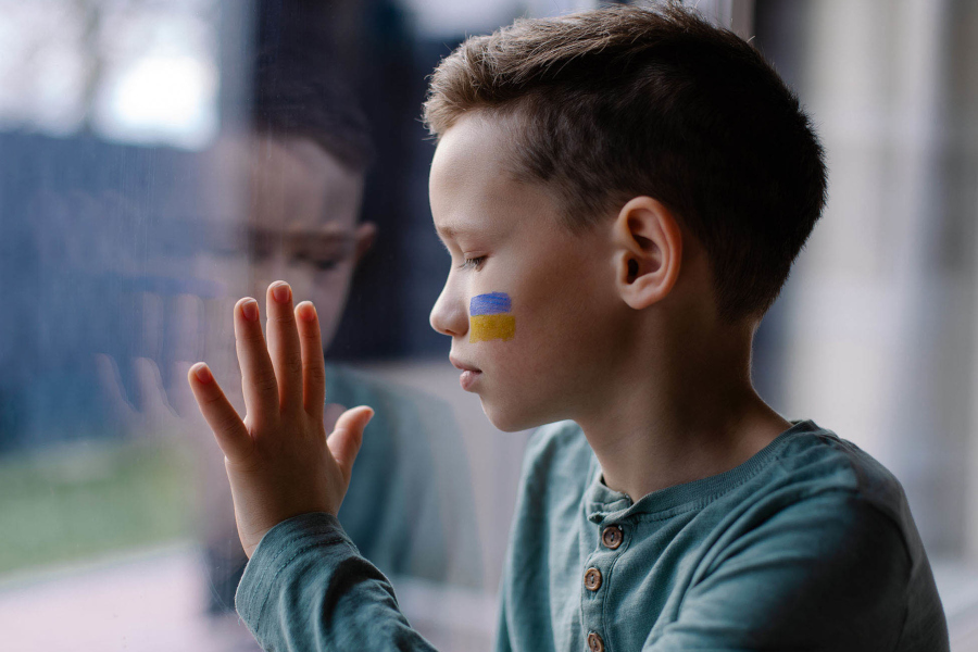 Zur ZSL-Seite Umgang mit dem Thema Krieg im Unterricht (Foto: Junge am Fenster mit Ukraine-Flagge auf der Wange)