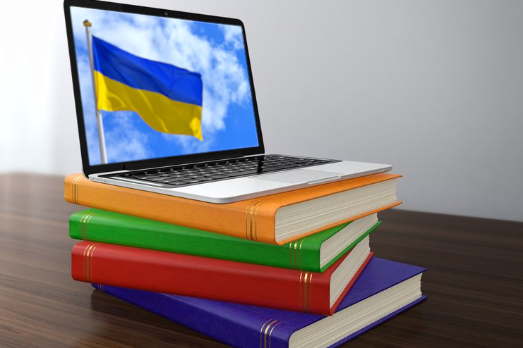 Link zur ZSL-Seite Ukrainische Schulbücher und Lernmaterialien (Foto: Laptop, auf dessen Monitor eine ukrainische Flagge zu sehen ist, steht auf einem Bücherstapel)