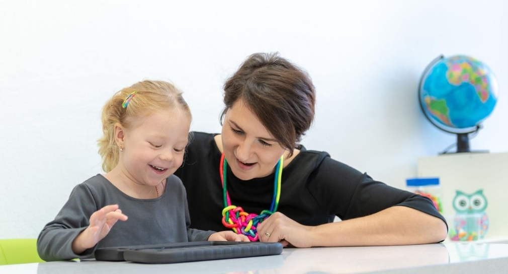 Foto: Sonderpädagogin mit Kleinkind; Kind kommuniziert mittels technischer Hilfe