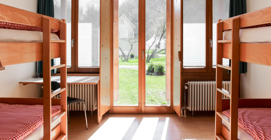 Foto: Schlicht eingerichtetes Gästezimmer mit zwei Stockbetten und Blick durch die gläserne Terrassentür ins Grüne.