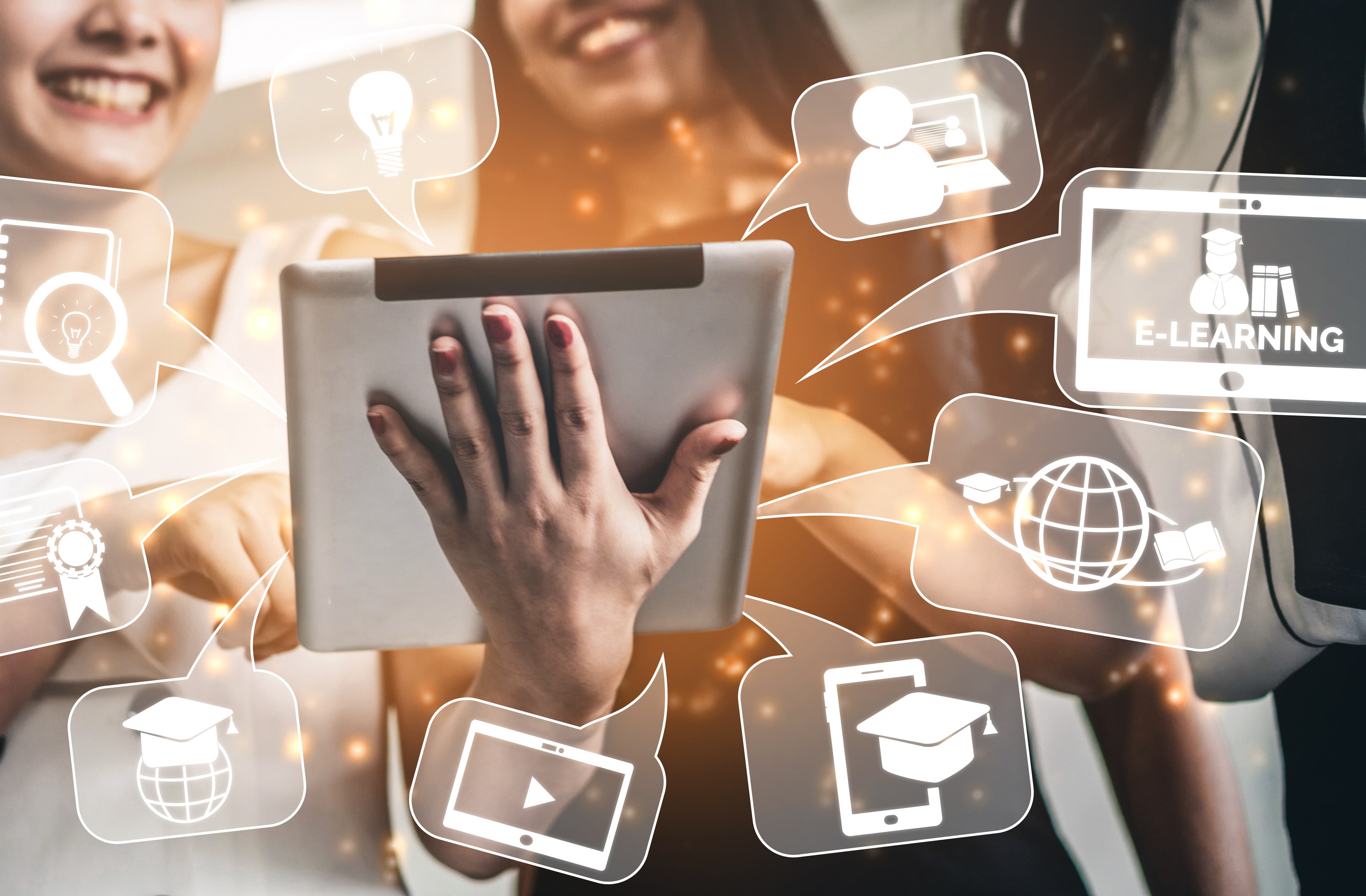 Zwei junge Frauen ein Tablet in der Hand haltend und darauf deutend, die Hand und das Tablet im Vordergrund, die Frauen leicht angeschnitten und unscharf im Hintergrund. Darum  angeordnet weiß-transparente Sprechblasen mit weißen Symbolen zum Thema Tablet und Internet.