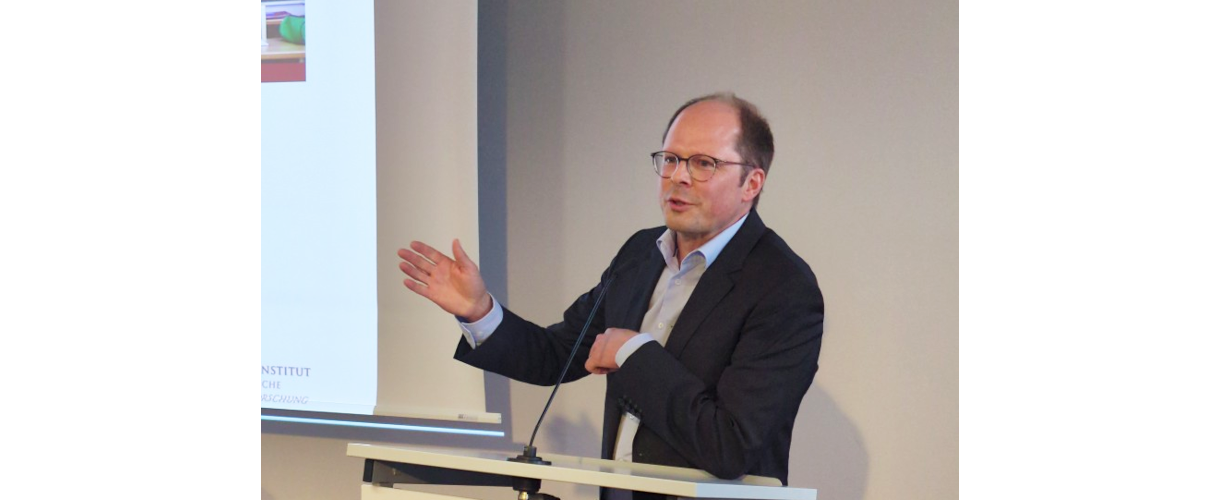 Fachtagung, Berlin 25.09.2025: Foto von Prof. Dr. Ulrich Trautwein (Er spricht am Rednerpult in das Mikro und gestikuliert mit den Armen. Er trägt Brille, ein schwarzes Jackett und ein weißes Hemd.)