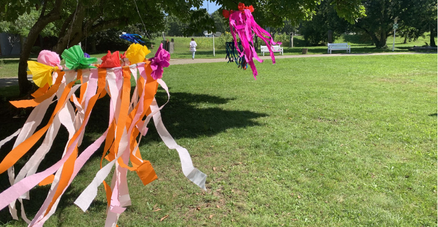 Link zur ZSL-Seite „Schülergrupppen Informationen“; Foto: Im Schlosspark wehen aus Krepppapier gebastelte, farbenfrohe Kränze im Wind.