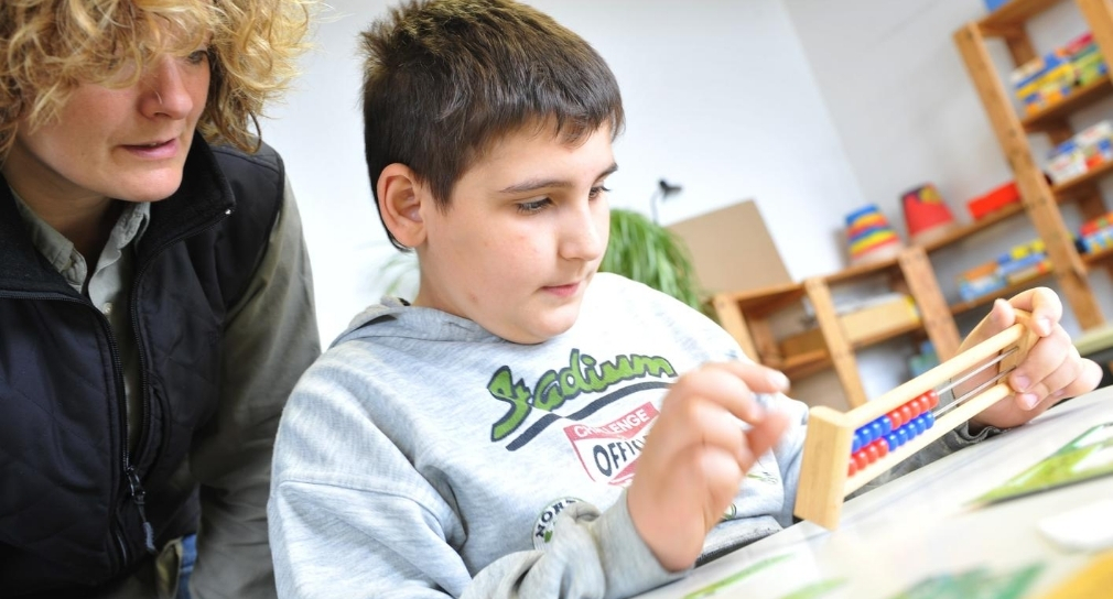 Foto: Lernbegleiterin beobachtet Schüler beim Rechnen mit dem Abakus