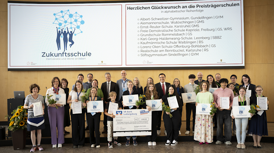 Foto von der Schulpreisverleihung „Demokratie und Werte (er)leben“ am 01.07.2024 im Stuttgarter Rathaus: Neben Lehrkräften und Schülerinnen und Schülern aus einer Preisträgerschule stehen auf der Bühne auch die Jury-Mitglieder, Kultusministerin Theresa Schopper, ZSL-Präsident Prof. Dr. Riecke-Baulecke und Schirmherr Prof. Dr. Wolfgang Reinhart (MdL).