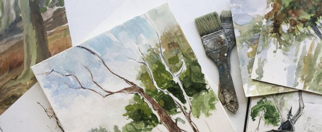 Mehrere Skizzen und Gemälde liegen auf einem Tisch, darunter eine Baumstudie in Blau- und Grüntönen, Zeichnungen, Pinsel und Zeichenstifte.