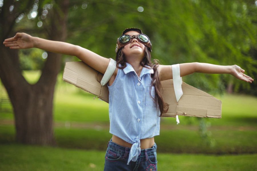 Link zur Seite Startchancen-Programm BW (Foto: Ein Mädchen steht auf einer grünen Wiese. Im Hintergrund ist ein Baum zu sehen. Das Mädchen trägt eine Fliegerbrille, Pappflügel, ein hellblaues mit Kragen und dunkelblaue Jeans. Es schaut nach oben und hat die Arme so ausgestreckt, als wolle es fliegen.)