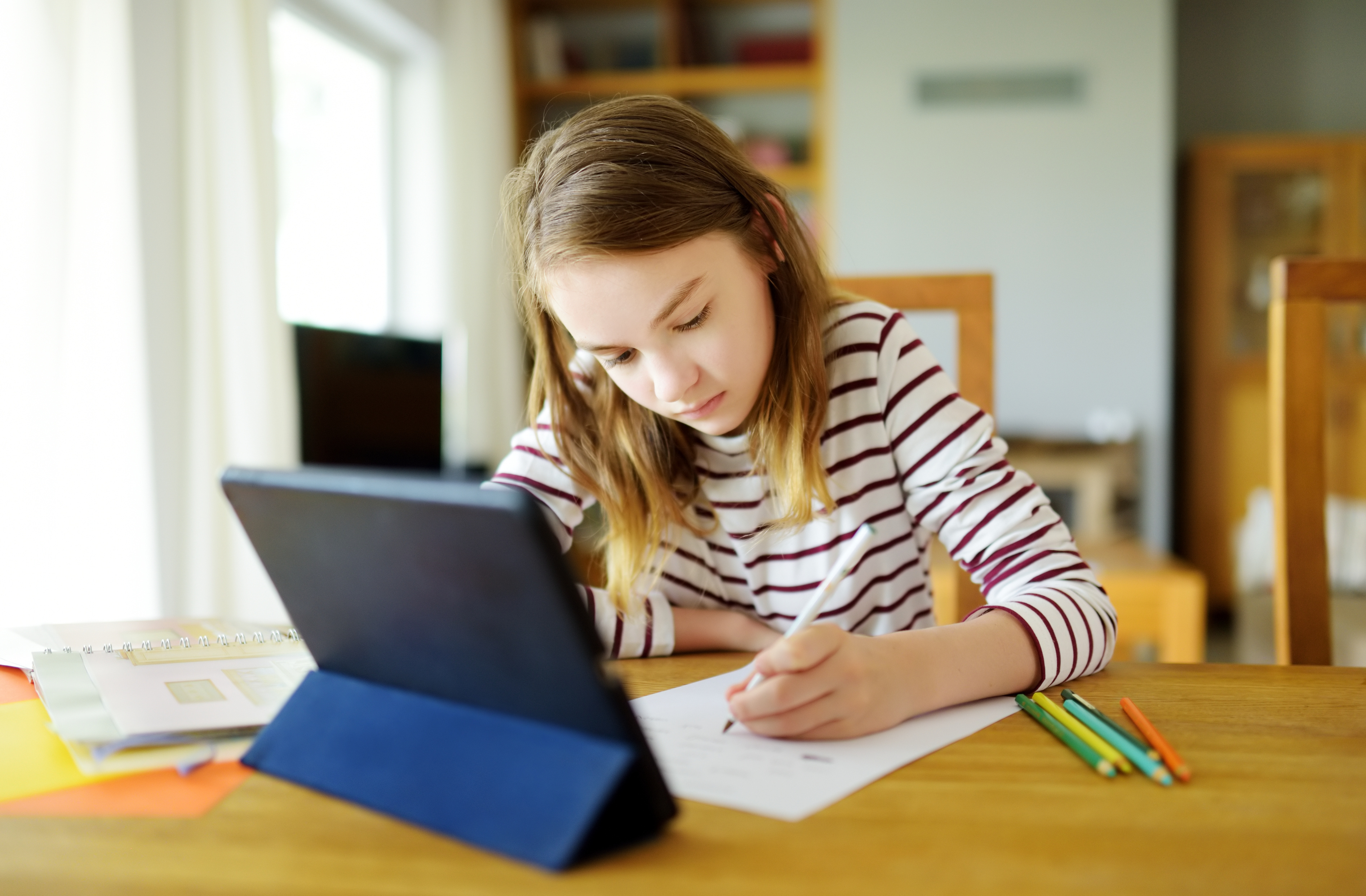 Mädchen arbeitet mit einem Tablet sowie mit Papier und Stift