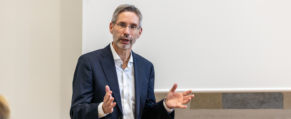 Vortrag von Prof. Dr. Jürgen Seifried, wissenschaftlicher Leiter des ZLBI der Universität Mannheim, anlässlich der Unterzeichnung des Kooperationsvertrags zwischen der Universität Mannheim und dem ZSL am 21. Oktober 2025 (Foto: Brustbild von Prof. Dr. Jürgen Seifried, der Brille, dunkelblaues Sakko und weißes Hemd trägt und die Arme angewinkelt hebt.)