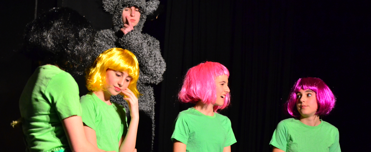 Foto einer Szene: Jugendliche mit bunten Perücken und grünen T-Shirts vor schwarzem Hintergrund