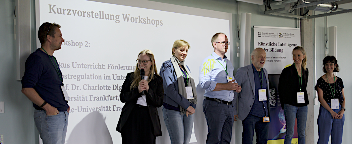 Foto vom 29. Juli 2025, Fachtag „Selbstregulation – zentrale Voraussetzung für erfolgreiches Lernen und Lehren“ am KI Zentrum Schule in Heilbronn: Folgende Personen stehen vor einer PowerPoint-Präsentation mit dem Folientitel Vorstellung der Workshops von links nach rechts: Dr. Tim Fütterer, Lea Nobbe, Nina Udvardi-Lakos, Prof. Dr. Tobias Renner, Dr. Gottfried Maria Barth, Dr. Isabel Brandhorst, Prof. Dr. Maria Theobald. Frau Nobbe hält ein Mikrofon und spricht Dr. Fütterer an. Die restlichen Personen schauen nach vorne.