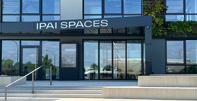 Foto: Außenansicht des Eingangsbereiches des IPAI-Spaces-Gebäudes in Heilbronn mit großen Fenstern und Sonneneinstrahlung