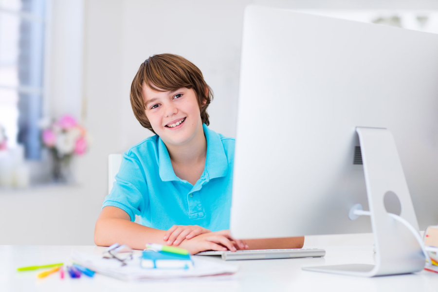 Link zur Seite Fernunterricht (Foto: junger Schüler im blauen Polohemd am Schreibtisch mit PC)