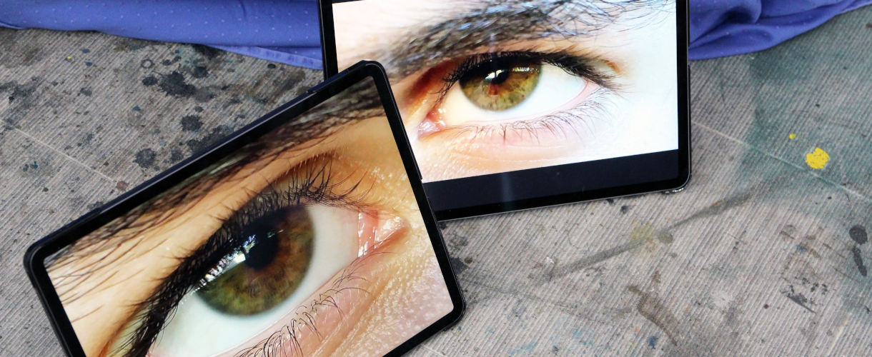 Foto: Zwei Tablets auf dem Boden zeigen Nahaufnahmen von Augen, die sich gegenseitig zu betrachten scheinen.