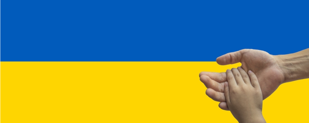 Foto: Kinderhand ruht in Erwachsenenhand, Hintergrund: ukrainische Flagge