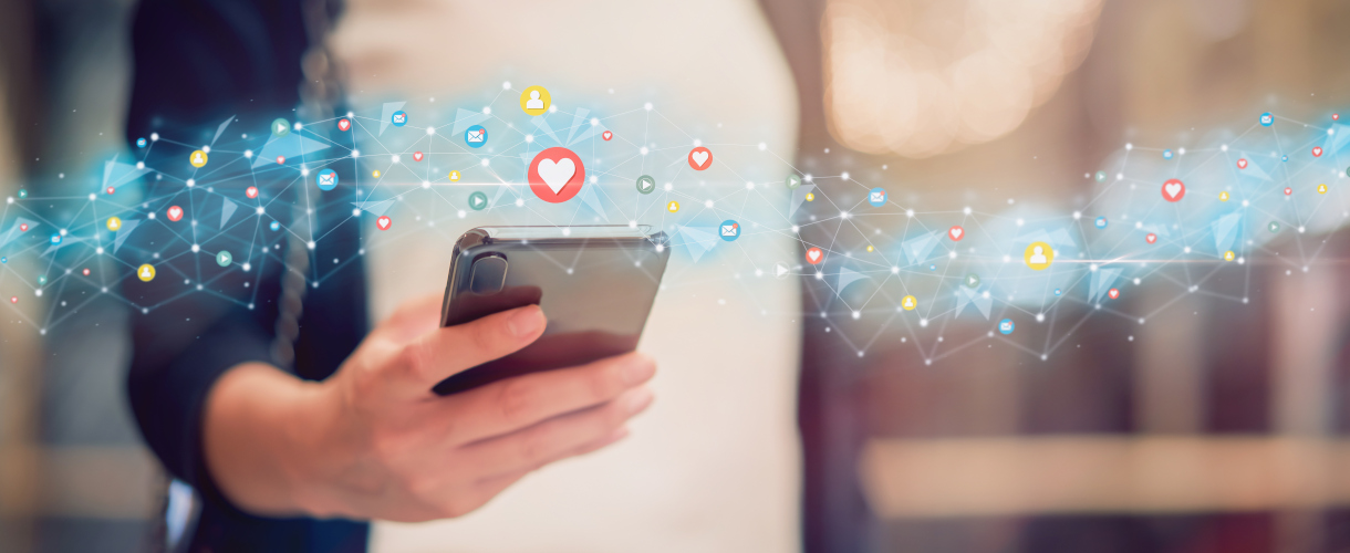 Link zur Aktuelles-Meldung: Unsere Schule im Zeitalter der Digitalität: Social Media, Smartphones und Selbstbestimmung (10. bis 12. Juni 2026) (Foto: Hand, die ein Smartphone hält; darüber fließt ein wolkenartiges Gebilde mit Icons für E-Mail, Liken, Anmelden und so weiter, die über ein Netzgeflecht verbunden sind etc.)
