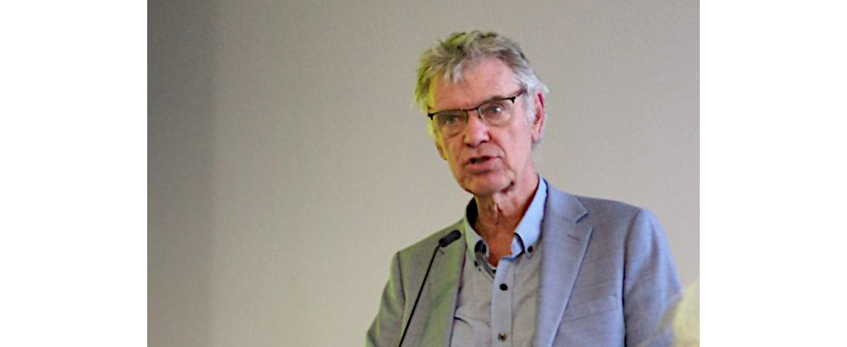 Fachtagung, Berlin 25.09.2025: Foto von Prof. Dr. John Hattie (Er spricht am Rednerpult in das Mikro. Er trägt Brille, ein graublaues Jackett und ein blaues Hemd mit aufgeknöpftem Hemdkragen.)