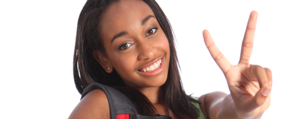 Sekundarstufe I (Jugendliche mit rotem Rucksack und grünem Top lächelt in die Kamera und macht mit der linken Hand das Victory-Zeichen).