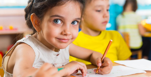 Foto: zwei Kinder im Grundschulunterricht: Mädchen im Vordergrund, Junge im Hintergrnd