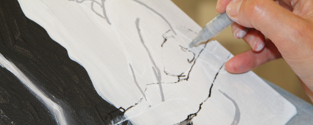 Foto von einer mit Filzstift zeichnenden Hand auf einem schwarz-weiß gemalten Bild.