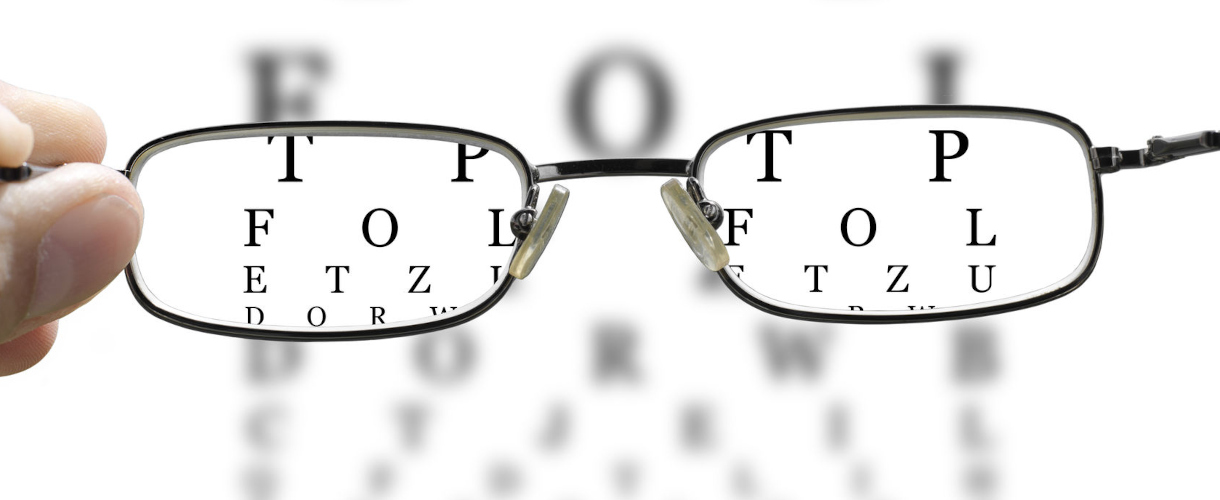 Im Fokus (Foto: eine vor eine Buchstabentafel gehaltene Brille fokussiert einzelne Buchstaben)