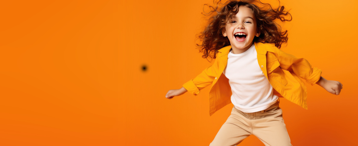 Foto: Fröhliches Kind mit lockigen Haaren springt vor einem orangefarbenen Hintergrund.“
