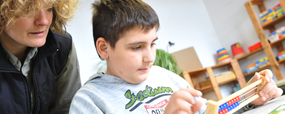 Foto: Lernbegleiterin beobachtet Schüler beim Rechnen mit dem Abakus