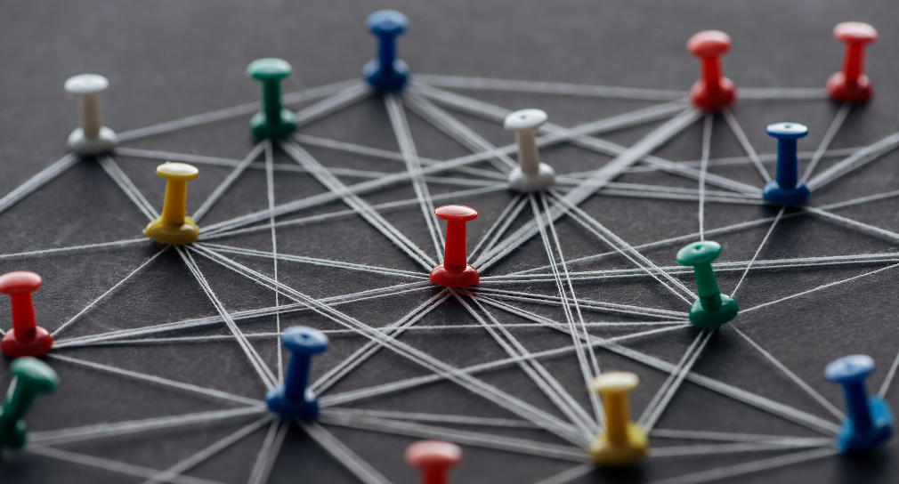 Symbolbild Kompetenzzentrum Schulpsychologie BW: Pins in den Farben weiß, grün, blau, rot und gelb sind gleichmäßig über eine graue Unterlage verteilt und durch Fäden verbunden.