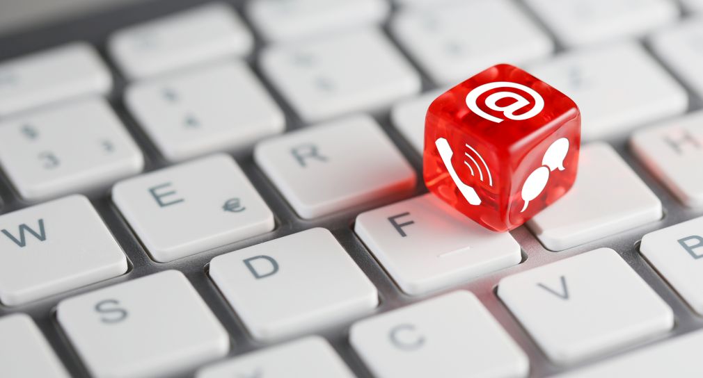 Link; Symbolbild Kontakte in die Regionen (Foto: Ein roter Kunststoffwürfel liegt auf einer Tastatur. Drei Flächen des Würfels sind sichtbar, auf denen ein Telefonhörer, das @-Zeichen und zwei Sprechblasen abgebildet sind.)