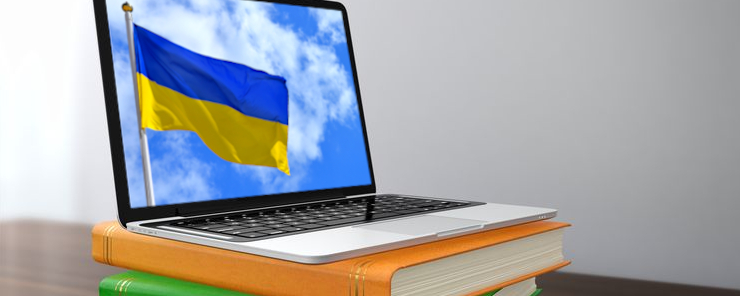Ukrainische Schulbücher und Lernmaterialien (Foto: Laptop, auf dessen Monitor eine ukrainische Flagge zu sehen ist, steht auf einem Bücherstapel)