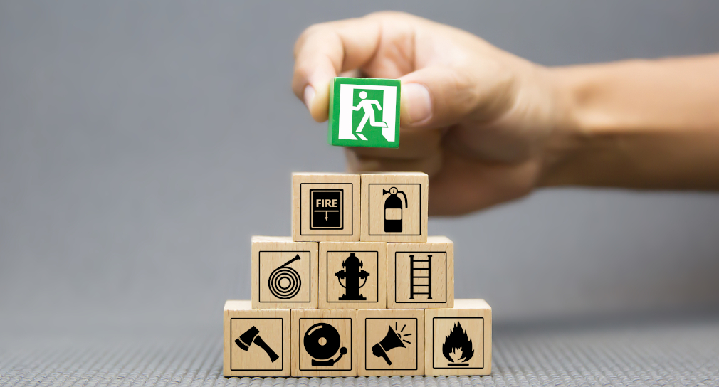 Symbolbild: Unterstützende Materialien (Foto: Hand legt ein Klötzchen mit Notausgang-Symbol auf einen Klötzchenturm)