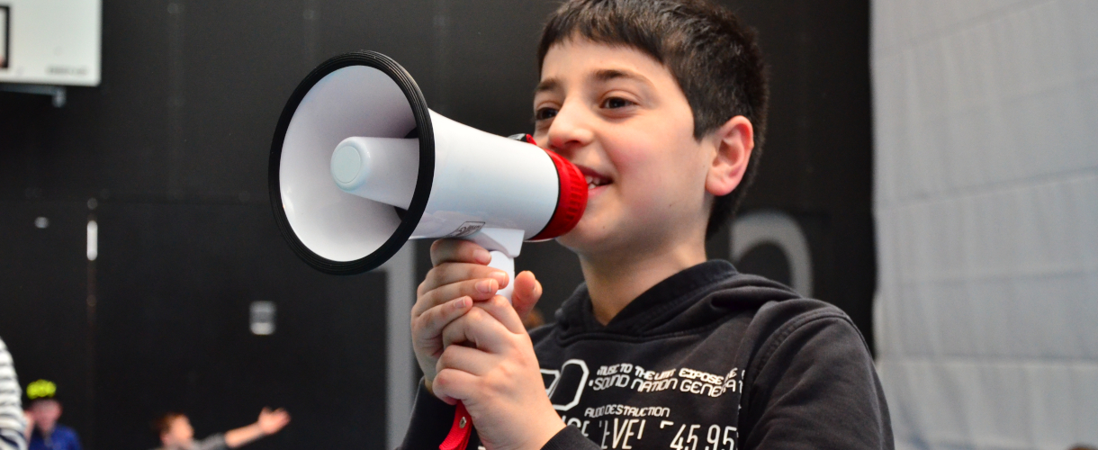 Foto: Din Junge spricht durch ein Megafon.