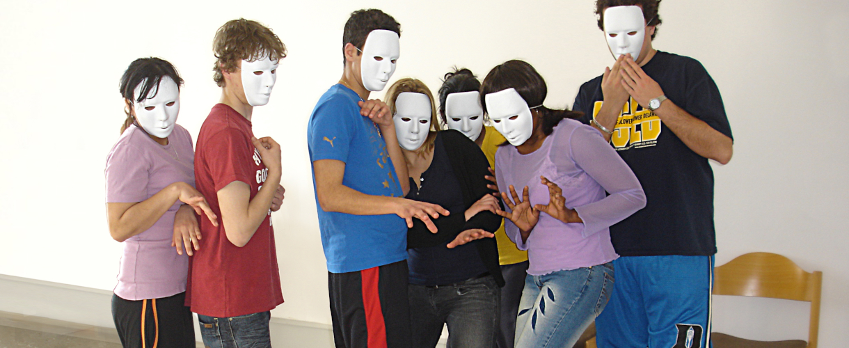 Foto einer Szene im darstellenden Spiel: Schülerinnen und Schüler mit weißen Gesichtsmasken