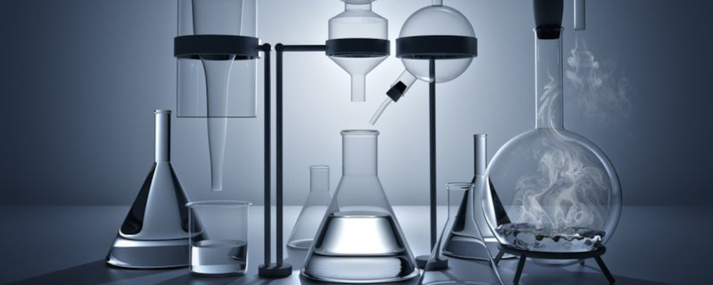 Symbolbild für Chemie (Foto: diverse gläserne Laborgefäße, zum Teil in Haltern, auf einem Tisch)