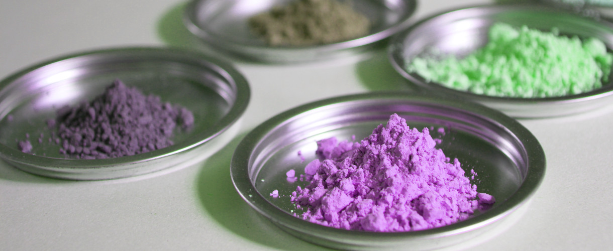 Foto: Mehrerer kleine Metallschälchen mit reinem Farbpigment in Violett, Grün und Braun.