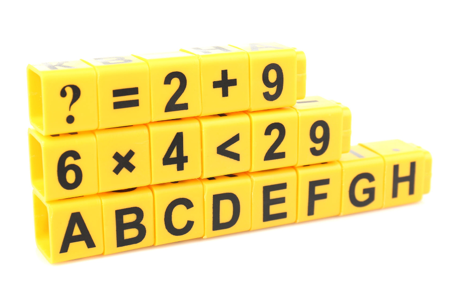 Link zur Seite Basiskompetenzen (Foto: drei übereinandergestapelte Reihen aus gelben Plastikbauklötzchen mit Ziffern, mathematischen Zeichen und Buchstaben; Inhalte der Bauklötzchen: oberste Reihe: ? = 2 + 9; mittlere Reihe: 6 x 4 < 29; unterste Reihe ABCDEFGH)