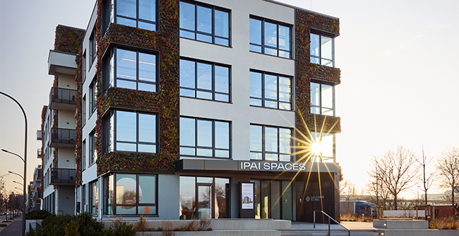 Foto vom IPAI-Gebäude: Außenansicht des IPAI-Spaces-Gebäudes in Heilbronn mit großen Fenstern und Sonneneinstrahlung am Eingang