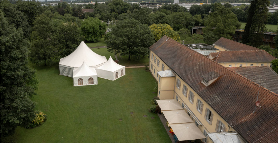 Luftaufnahme von der Parkanlage mit einem langgezogenen Schlossgebäude und einem weißen Pagodenzelt mit Spitzdach und zwei angeschlossenen Nebenzelten.