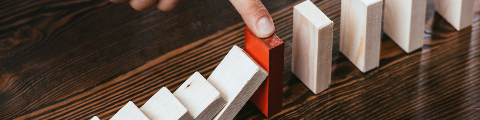 Foto: Hand stoppt das Umfallen einer Dominoreihe (Symbolbild: Prävention)